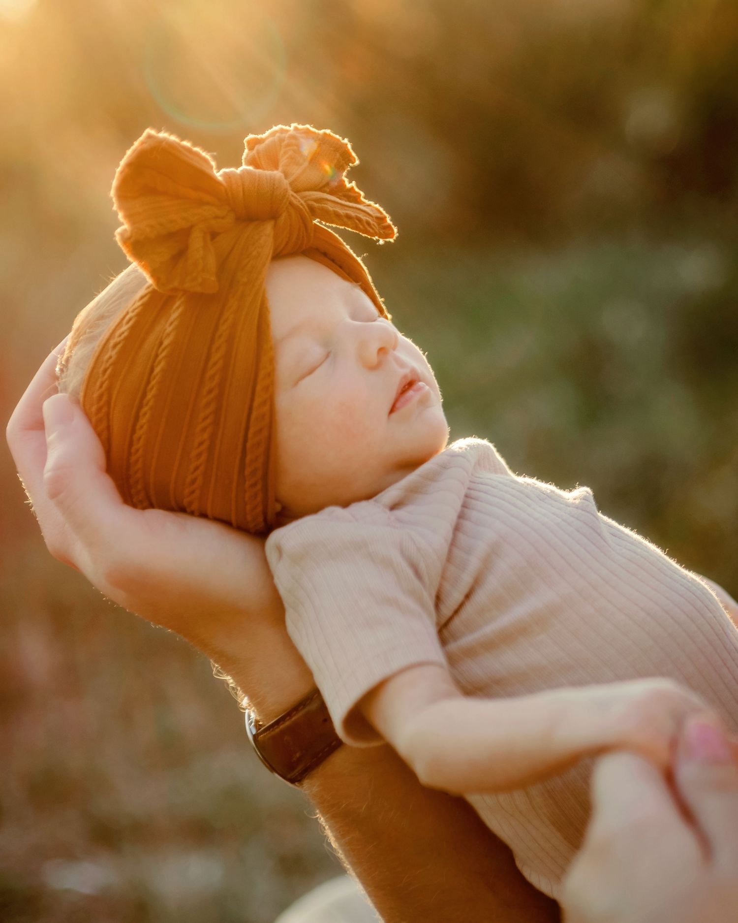 A newborn baby is held up with the golden hour sunlight shining down, creating a dreamy backlit glow in Fort Worth, TX.
