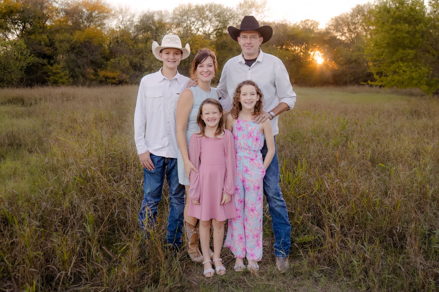 Western-style group portrait in a rustic field at golden hour with tall grass and autumn trees in background.