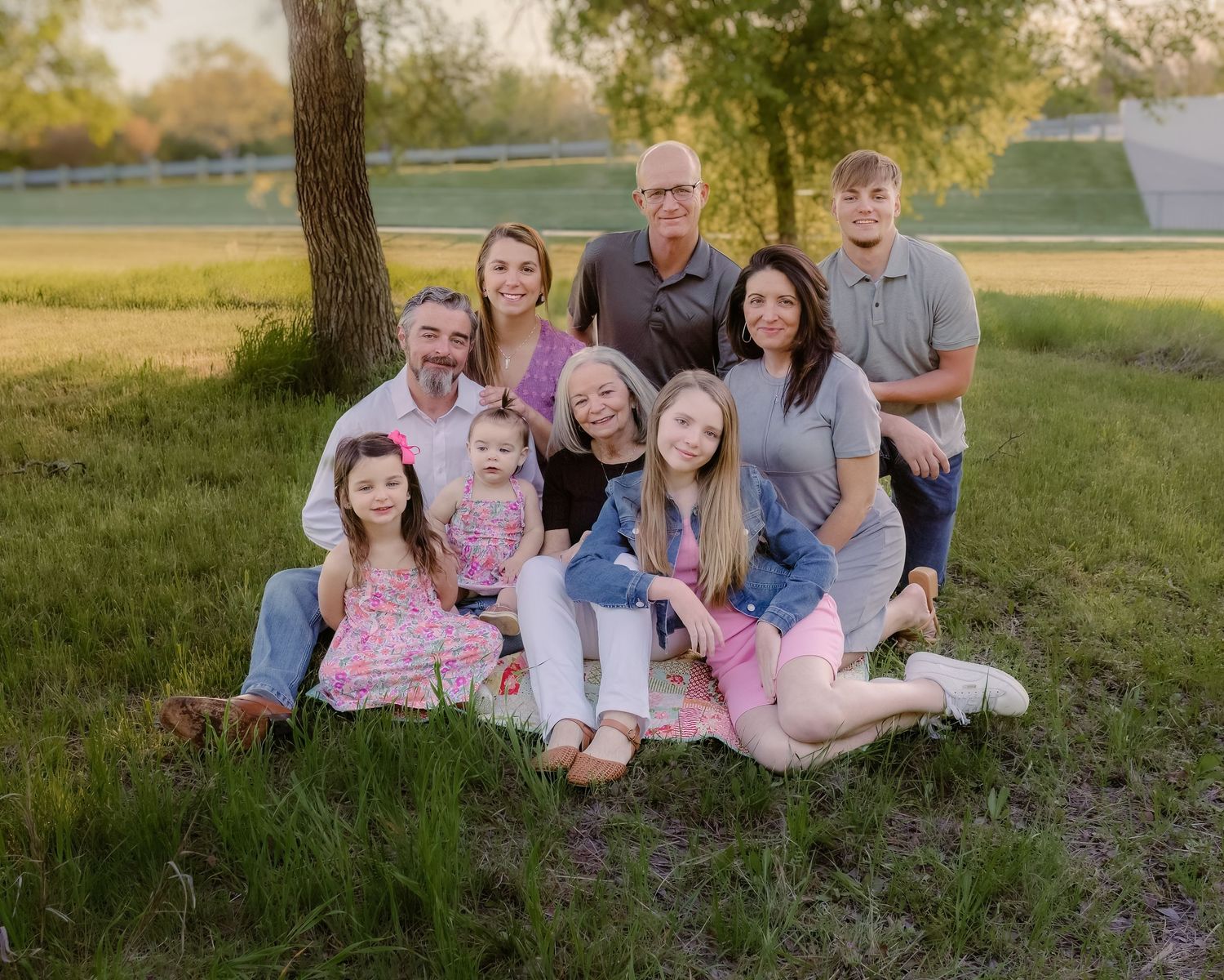 Large family group posed together outdoors under trees during golden hour.