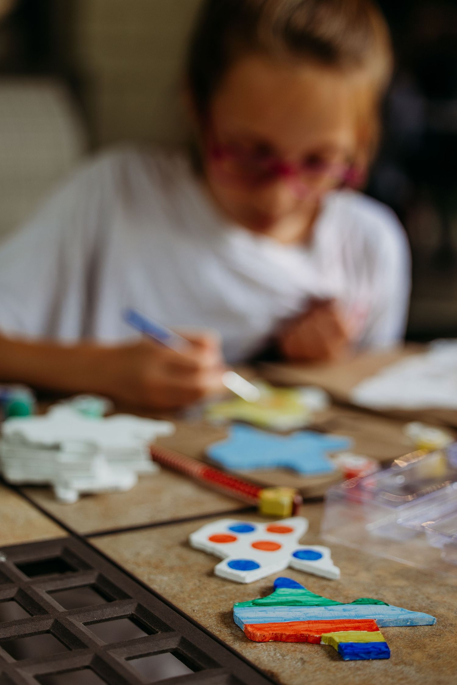 Child focused on painting colorful star-shaped ornaments with watercolors while seated at wooden table in Springtown, TX