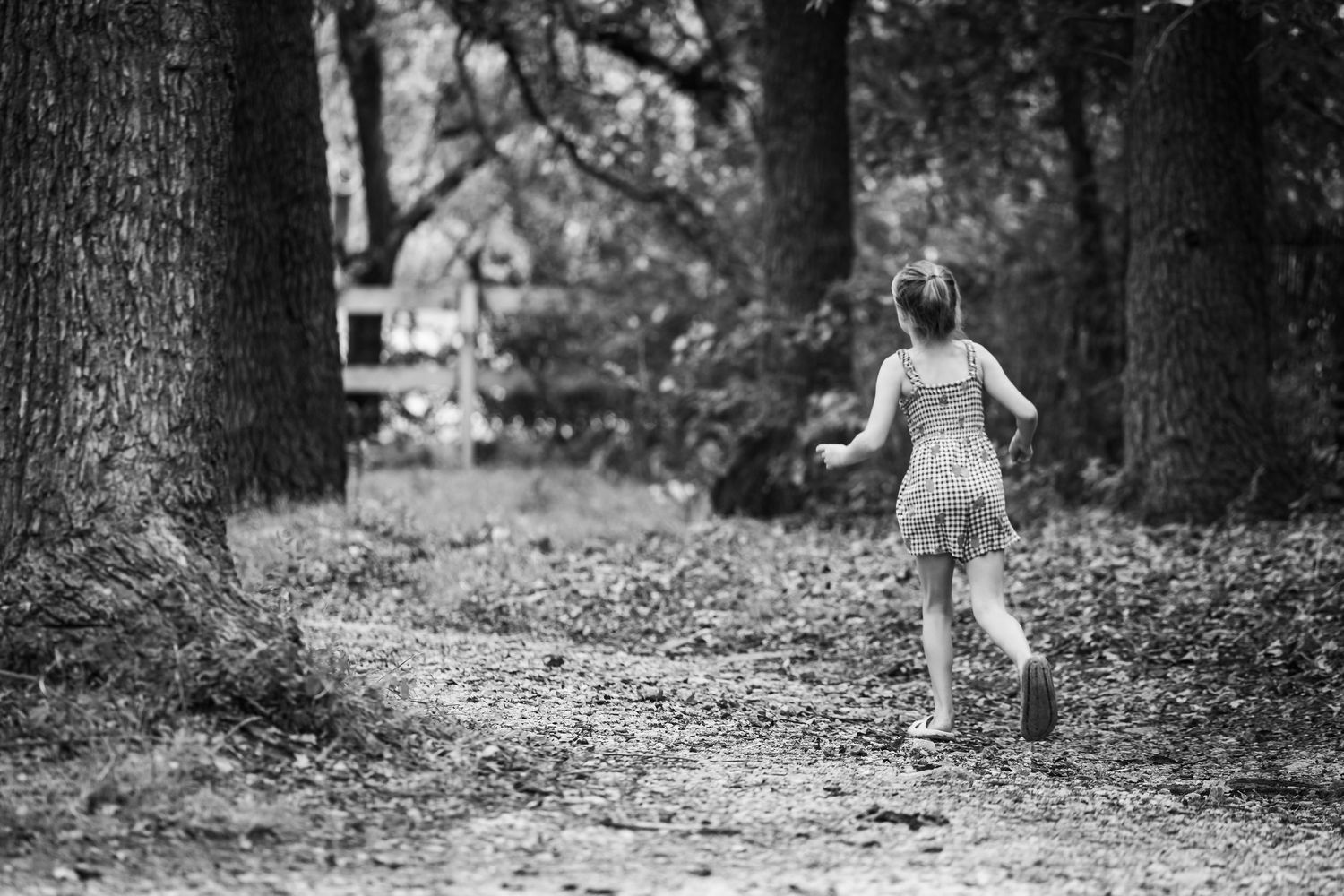 A child in a dress runs through a wooded area in black and white, creating a dreamy nostalgic scene.