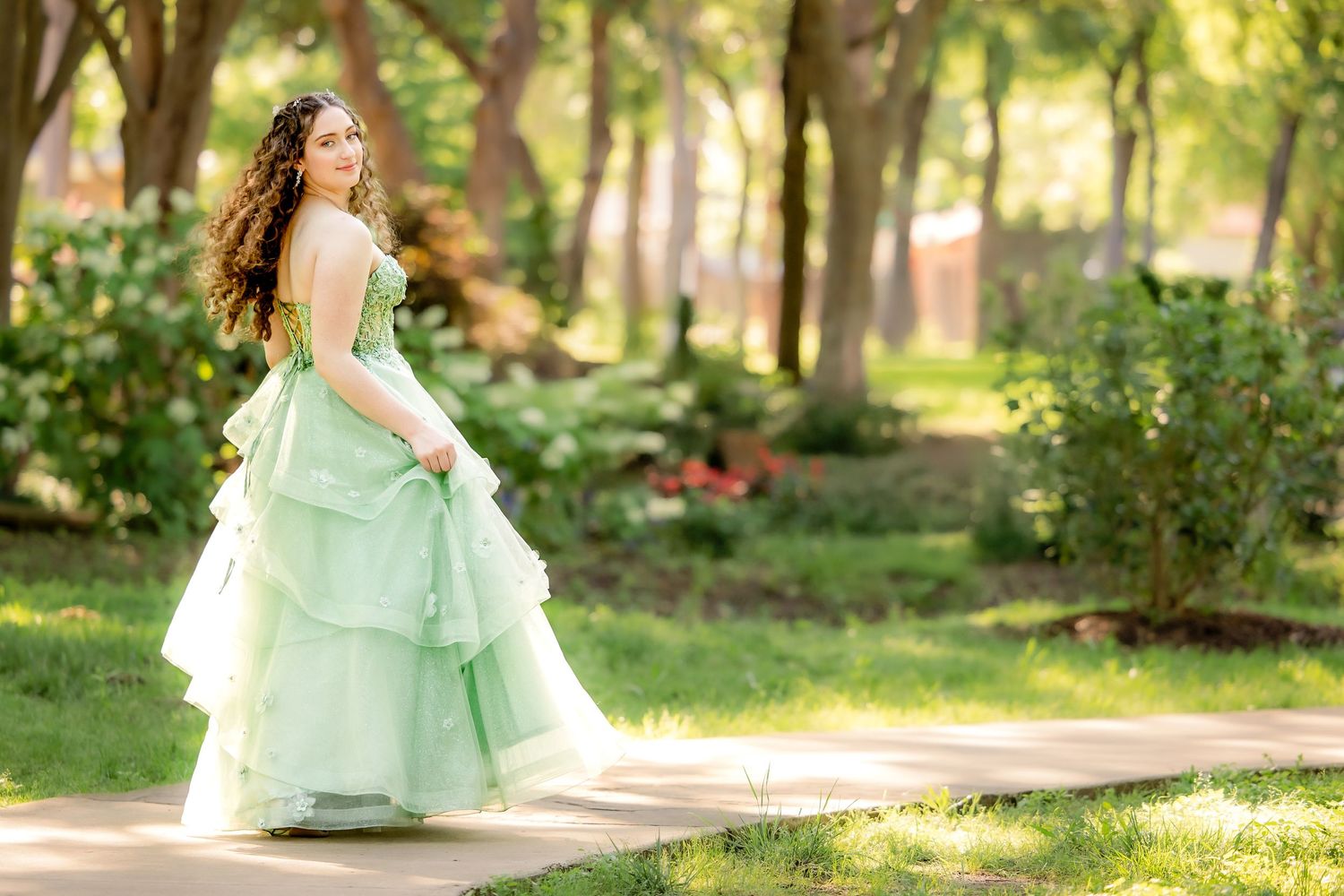 A person in a flowing mint green gown twirls gracefully in a sunlit garden setting.