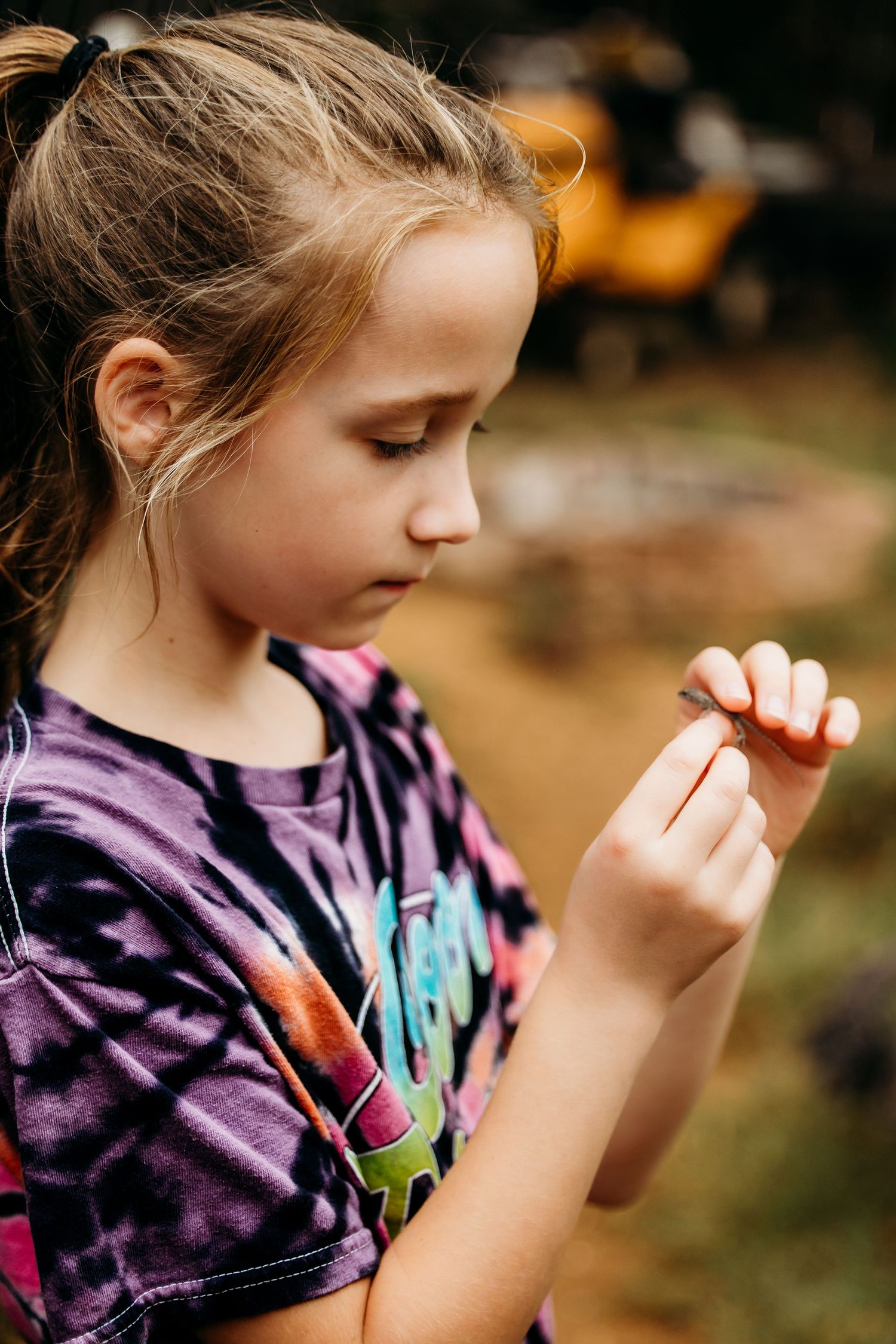 Young person wearing tie-dye shirt examines something small with curiosity in Keller, TX.
