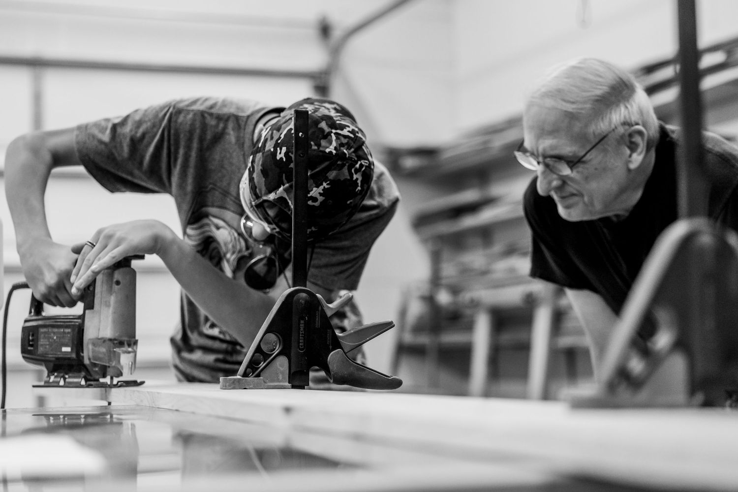 Black and white photo showing two craftsmen working together with tools at a workshop table.