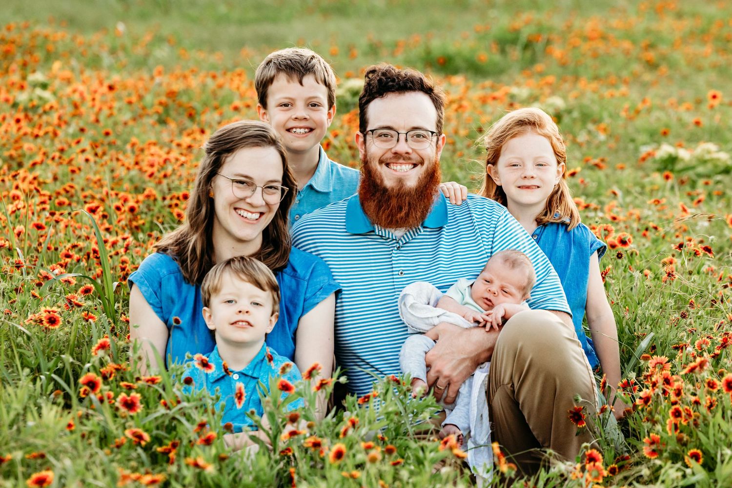 Family of six sitting together in a vibrant field of orange wildflowers on a sunny spring day in Fort Worth, TX.