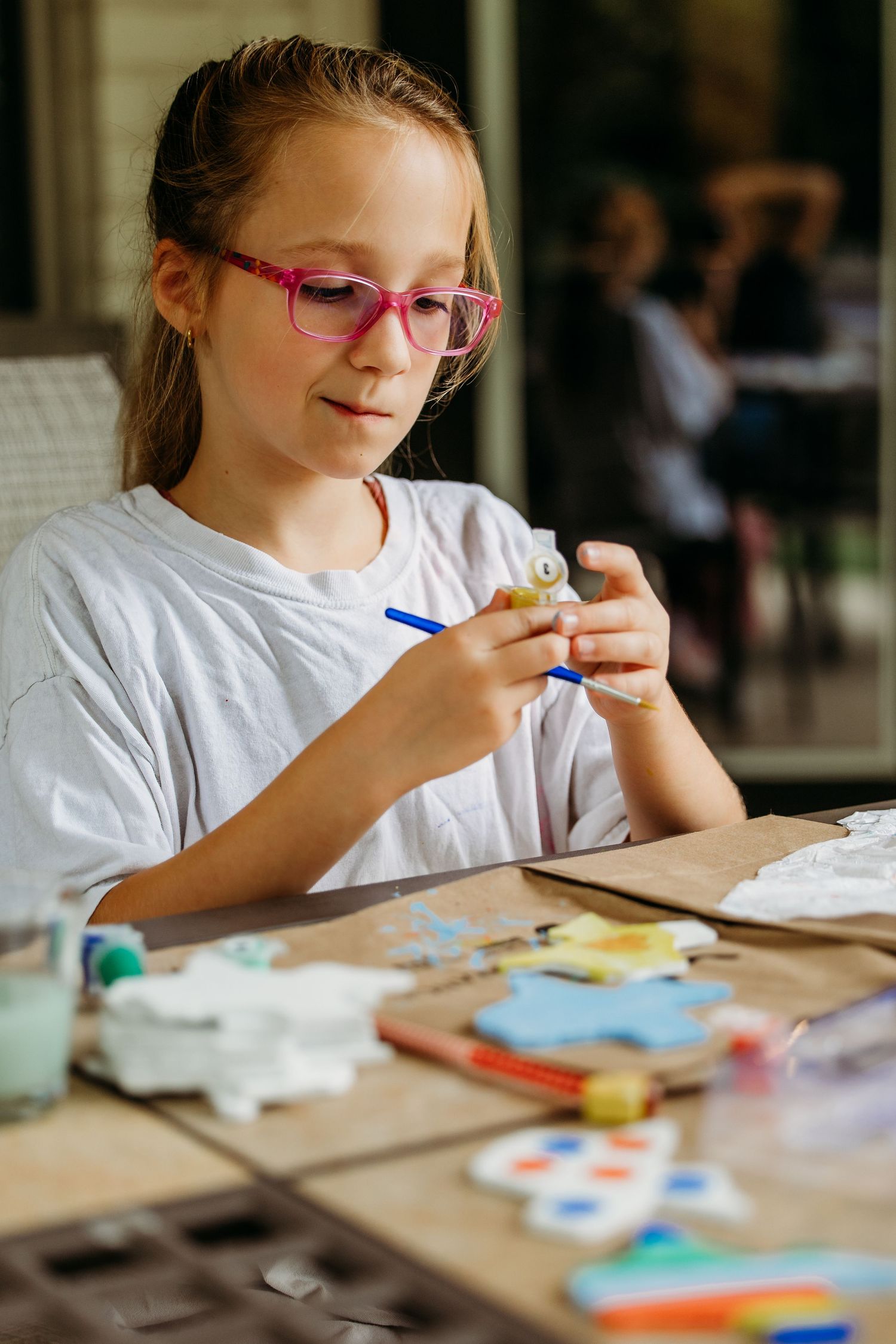 A student wearing a white shirt and red glasses focuses intently on an art project or drawing at a wooden desk in Springtown, TX