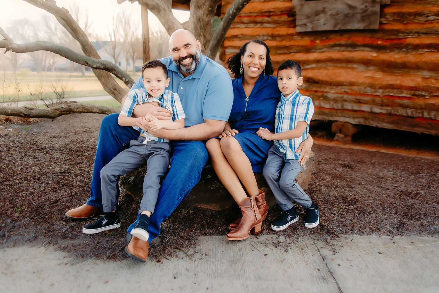 Family sitting together on rustic wooden steps during outdoor photo session in casual denim and blue outfits.