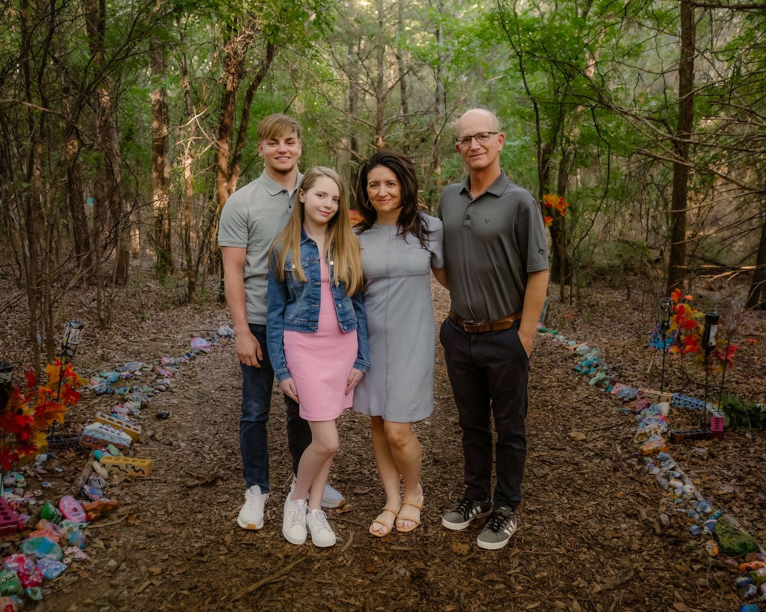 Group portrait in wooded area with decorated path and colorful flowers.