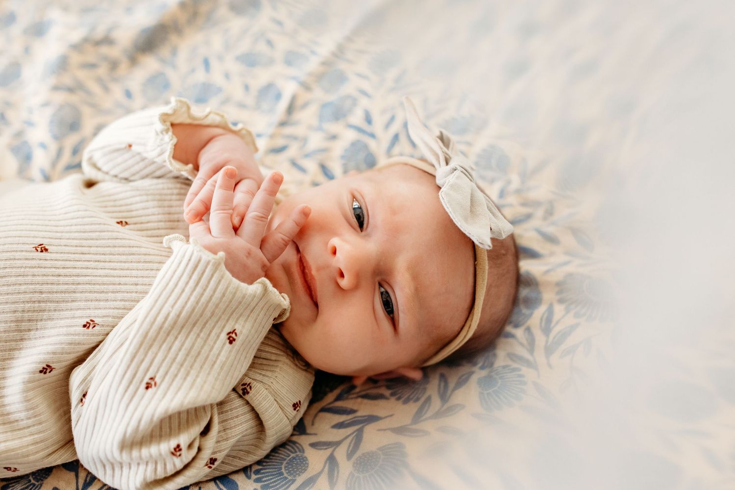 Baby wearing cream knit sweater and white bow headband lies on lace blanket.