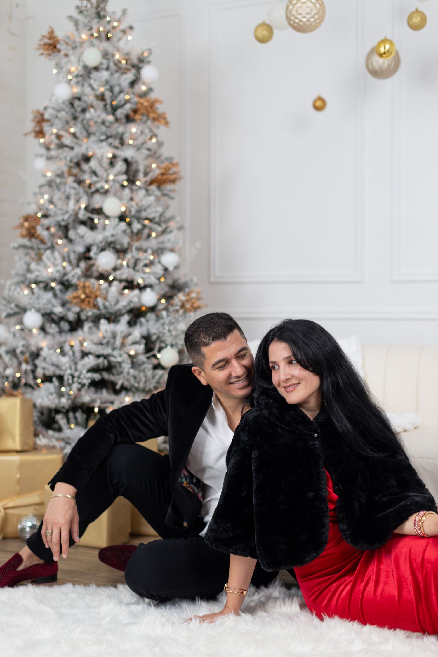 Four romantic holiday portraits show a couple in formal black and red attire posing by a decorated white Christmas tree.