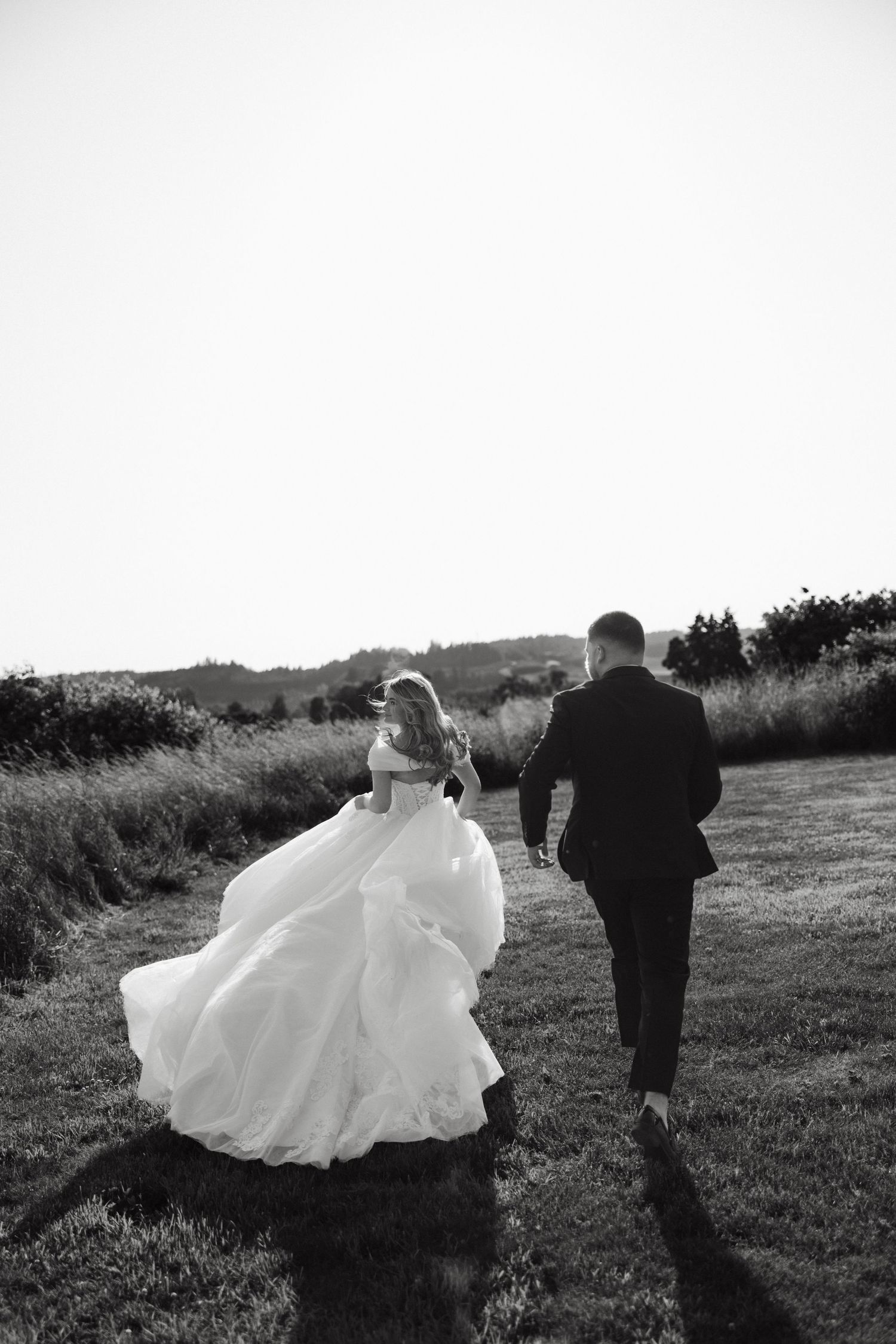 Black and white sequence of four wedding photos showing a couple walking through a grassy field, bride's dress flowing in the wind.