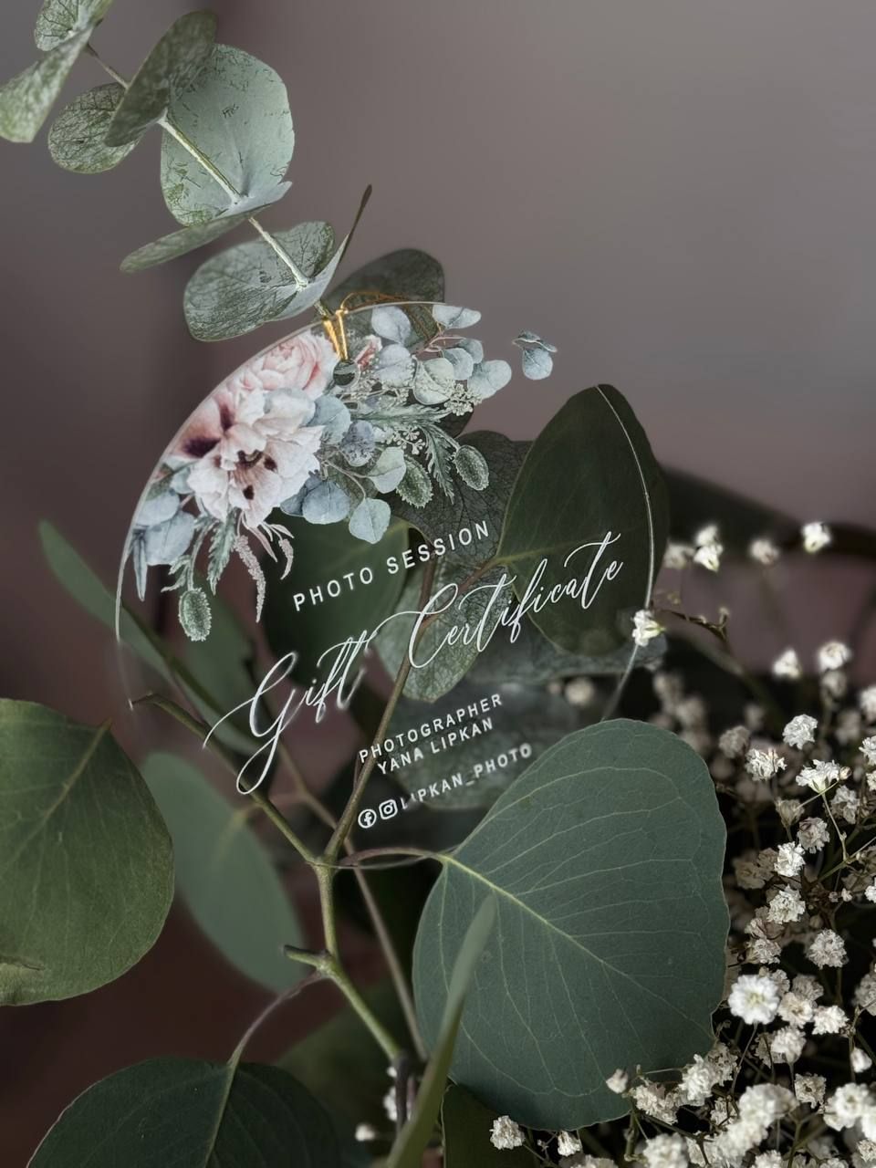 A photo session gift certificate decorated with eucalyptus leaves and baby's breath flowers.