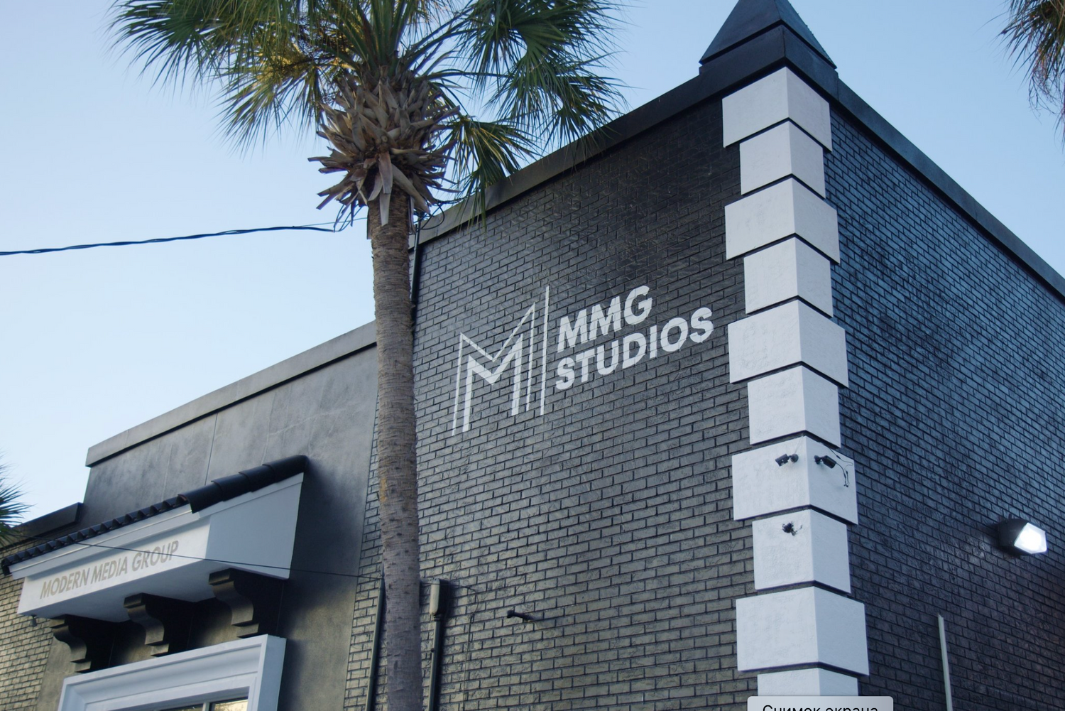 Modern brick building exterior with MMG Studios signage and palm tree against blue sky.