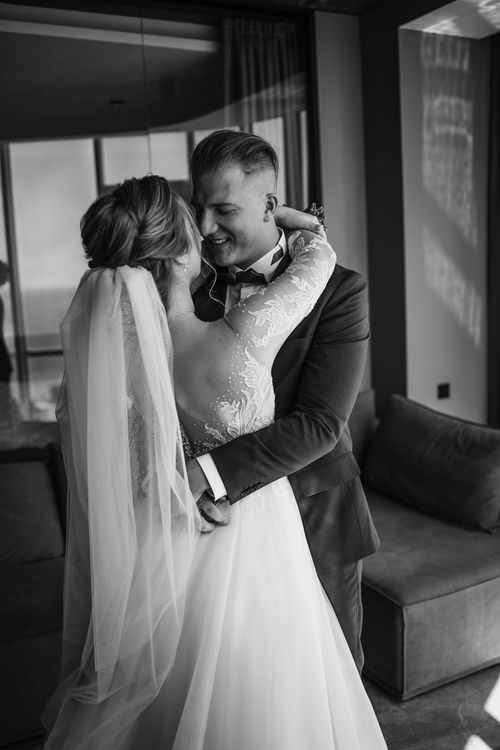 Intimate black and white photo of newlyweds sharing a tender moment indoors.