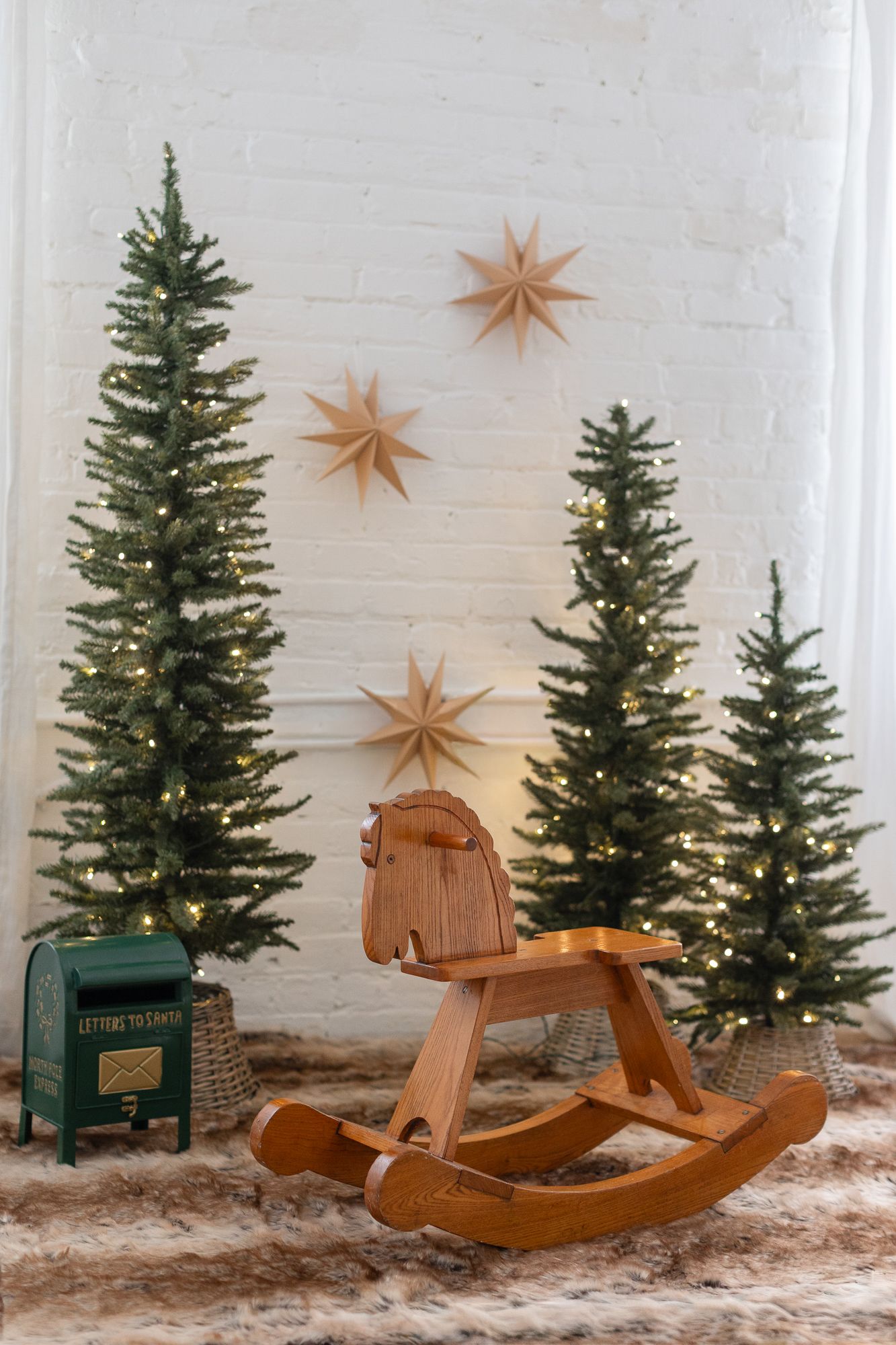 Three wooden rocking horses are displayed with small Christmas trees and star decorations against a white wall.