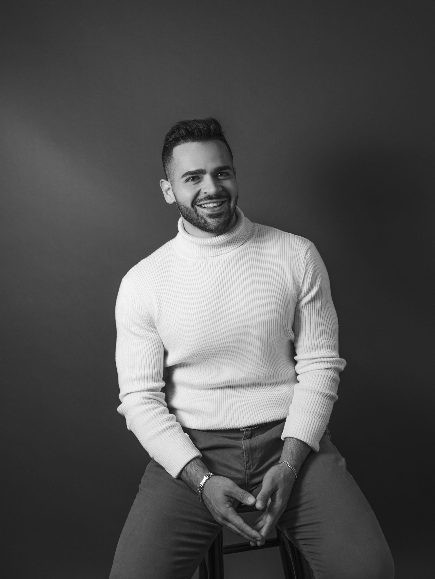 Man in white turtleneck sweater smiles during black and white portrait session.