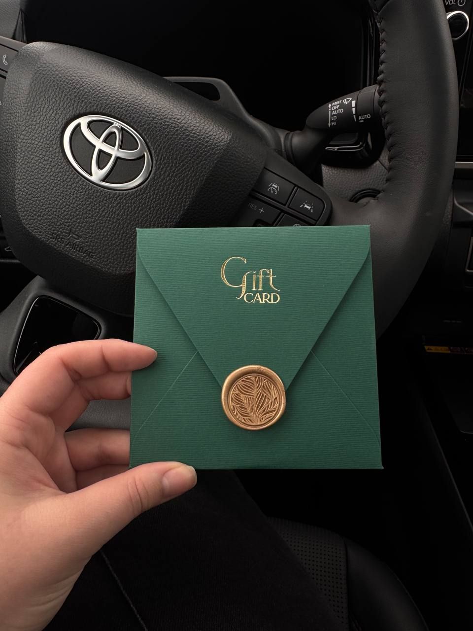 An elegant green envelope with golden wax seal displayed on a Toyota car dashboard.