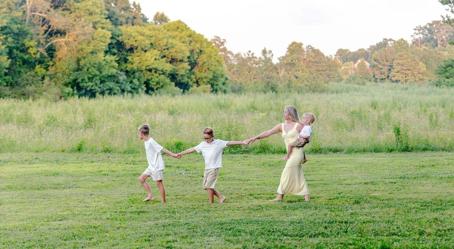 Family Photos Calhoun GA Family holding hands and playing in a green meadow with trees in the background on a sunny day.