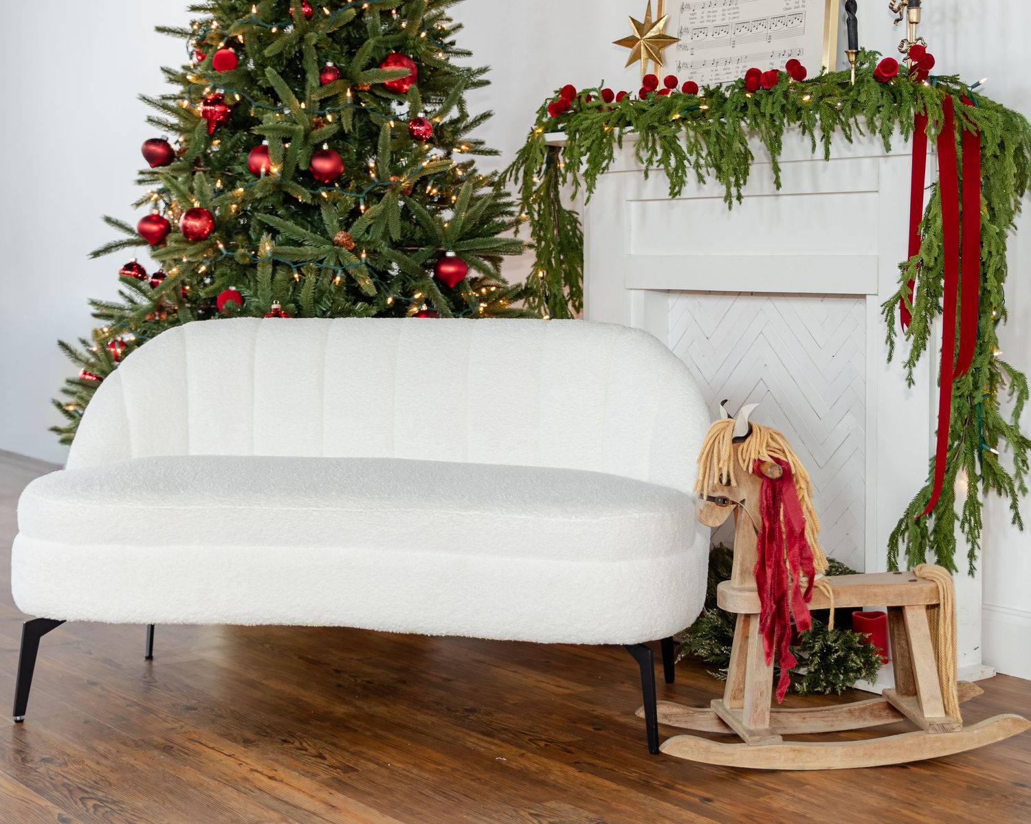 White velvet sofa beside a wooden rocking horse near a decorated Christmas tree and garland-adorned fireplace.
