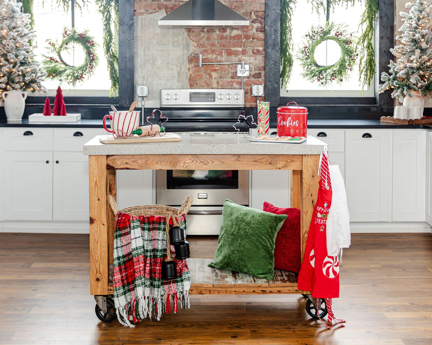 Festive kitchen with Christmas wreaths, plaid blanket, green pillow, and holiday decor on a wooden island.