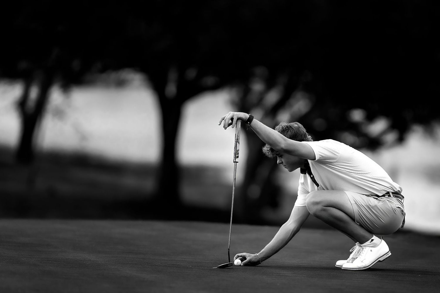 Golfer crouching to read the green in black and white photography on a golf course.