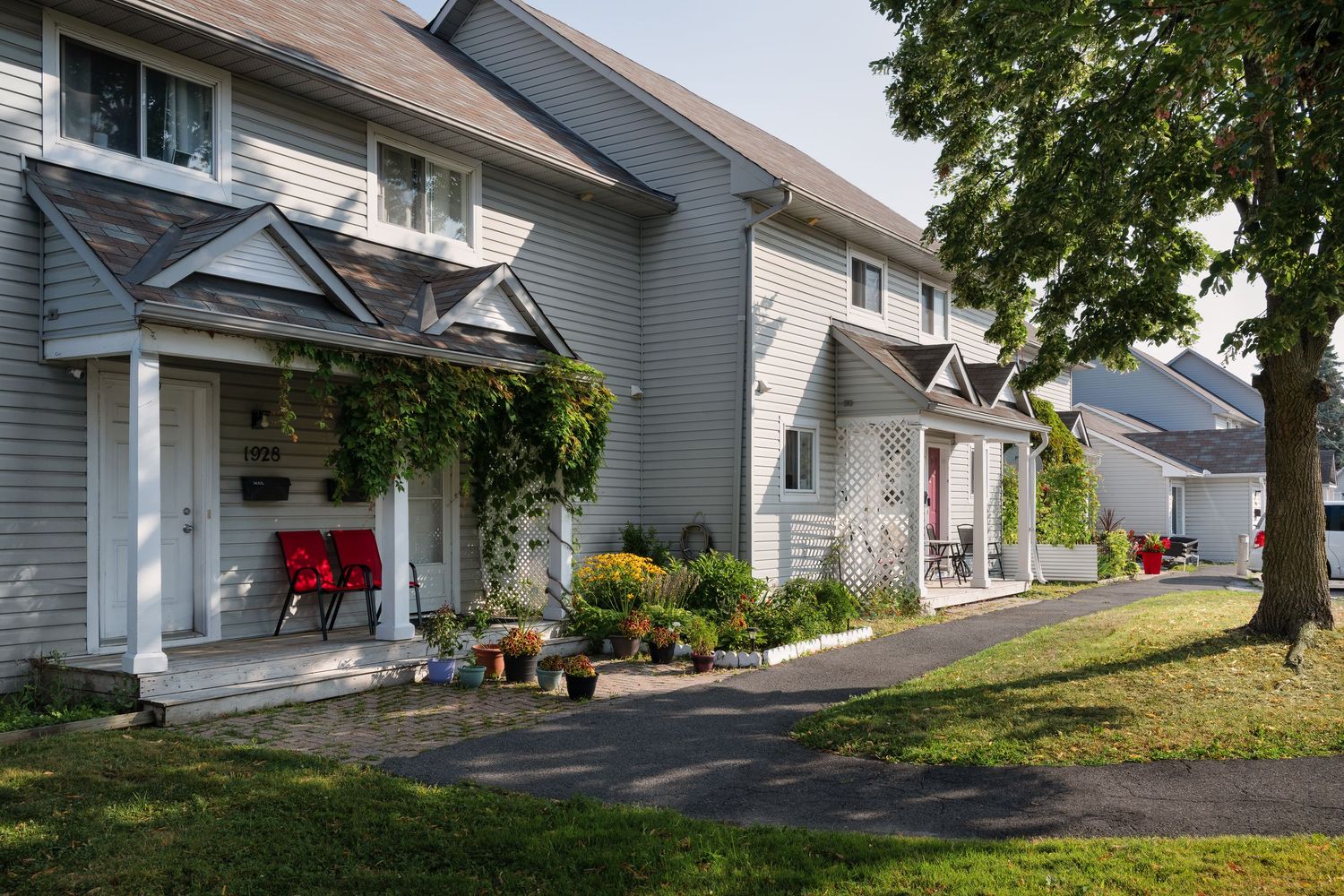 White houses with driveways and garages line a gently curving suburban street with mature trees.