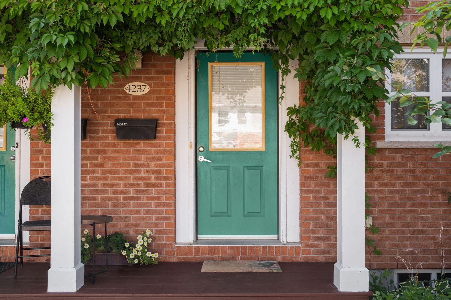 Brick row house with green doors and white columns feature overhanging tree branches along a residential street.