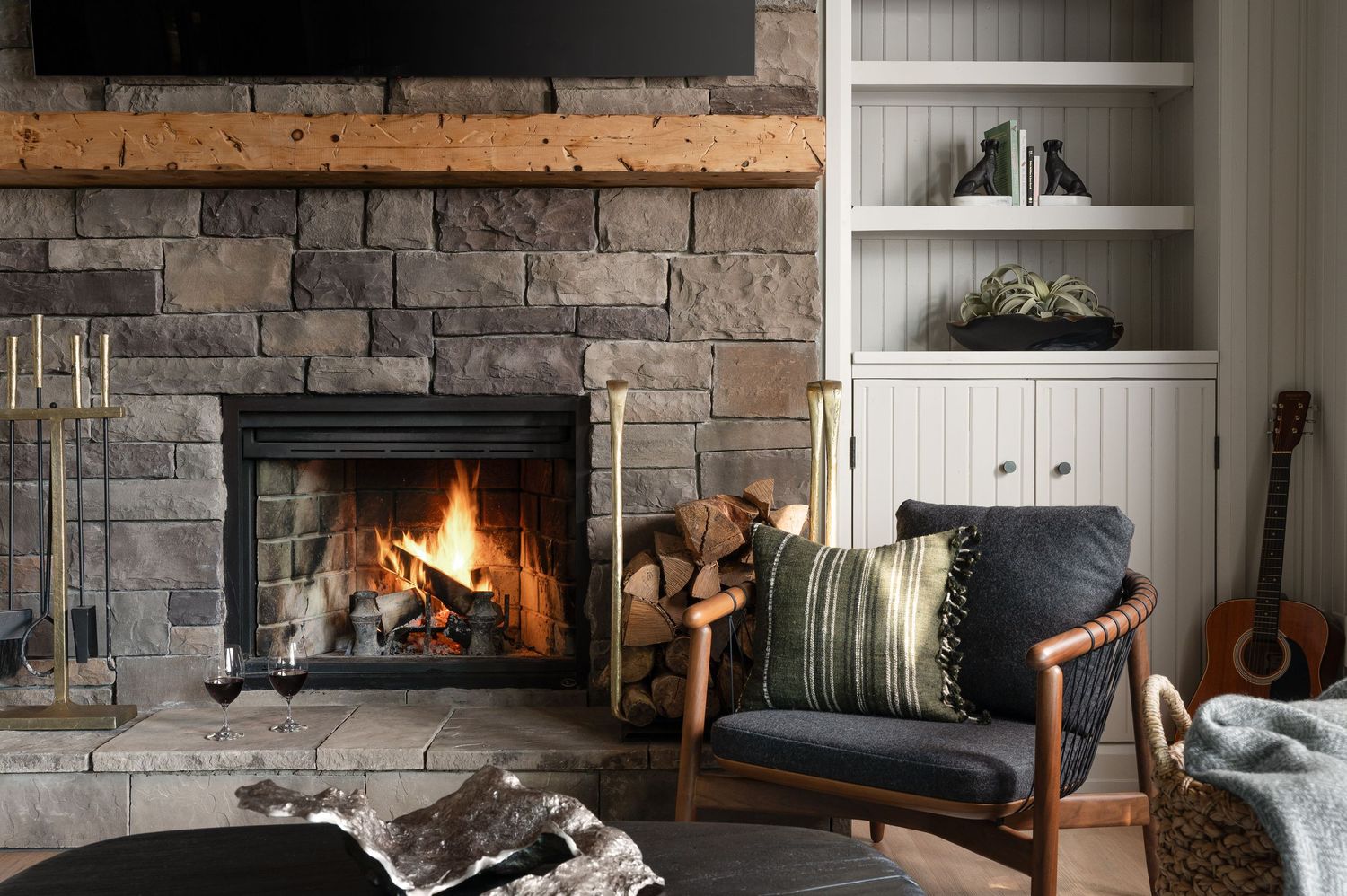Rustic stone fireplace with burning logs, flanked by built-in shelving and comfortable seating.