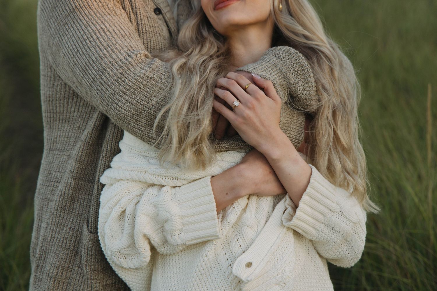 Close up of couple embracing in a field wearing cozy knit sweaters with warm tones and gentle lighting.