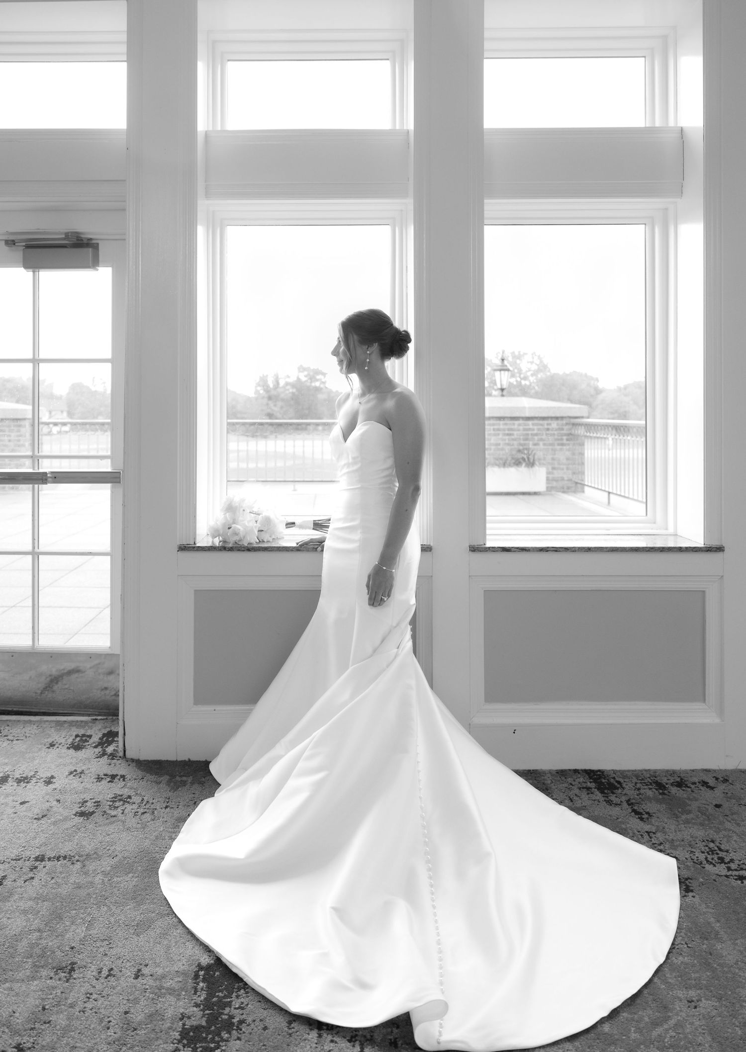 Elegant bridal portrait silhouetted against bright windows showing dramatic train of white wedding gown.