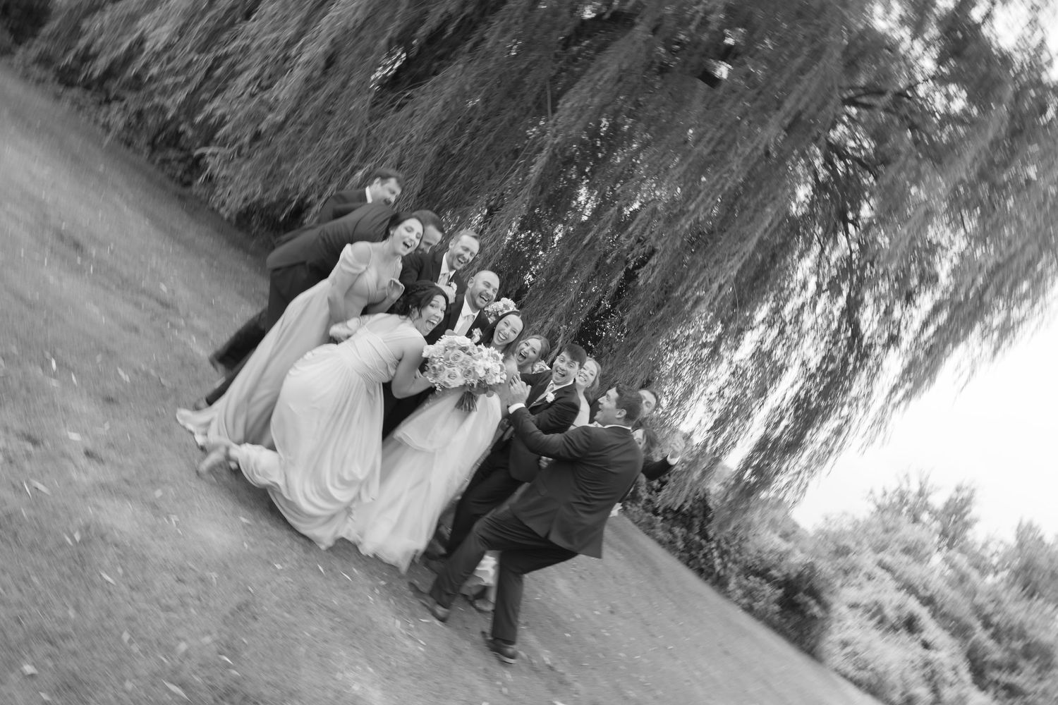 Black and white candid photo of wedding party sitting together on rocky beach slope.