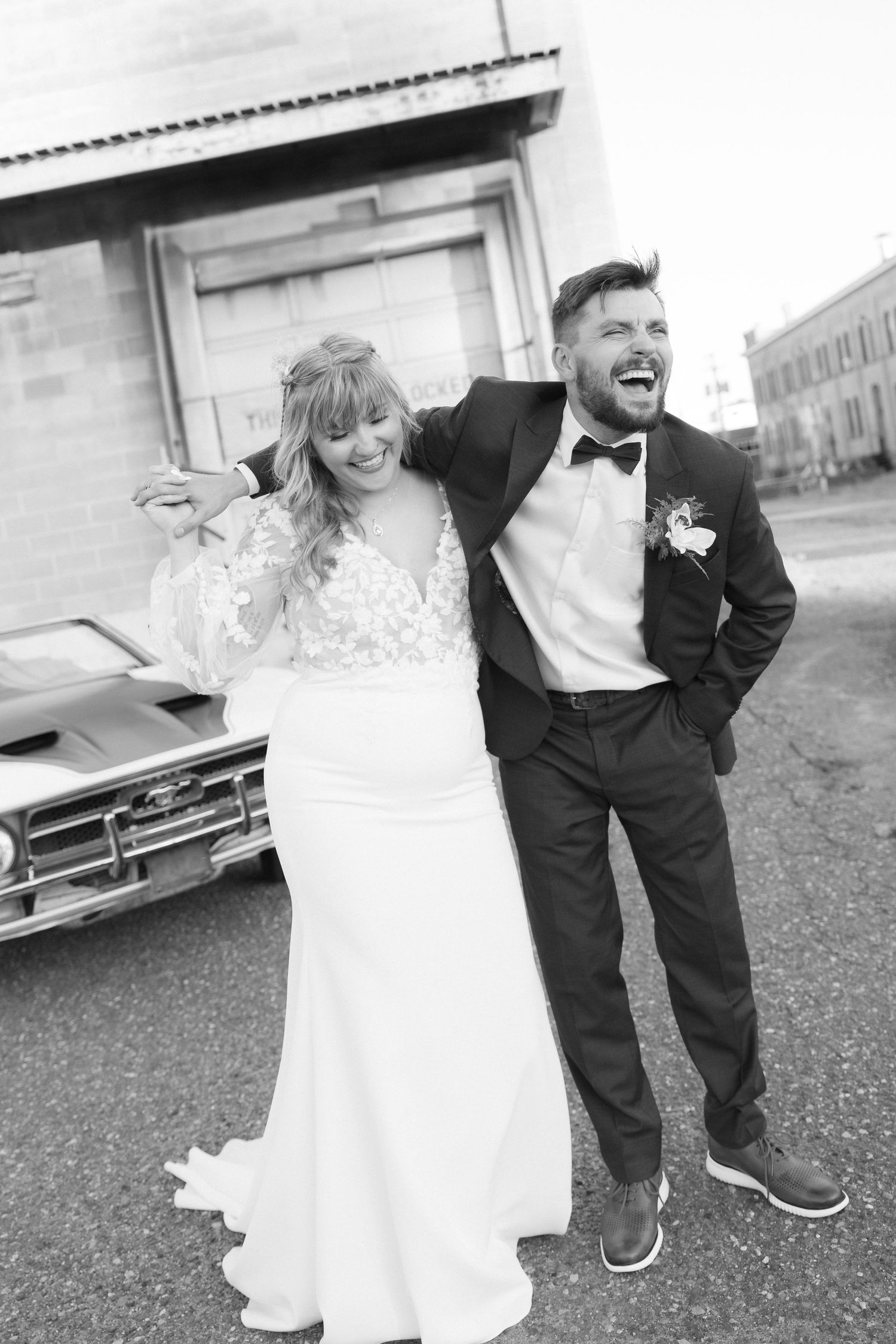 Candid black and white photo of joyful newlyweds laughing together outdoors.