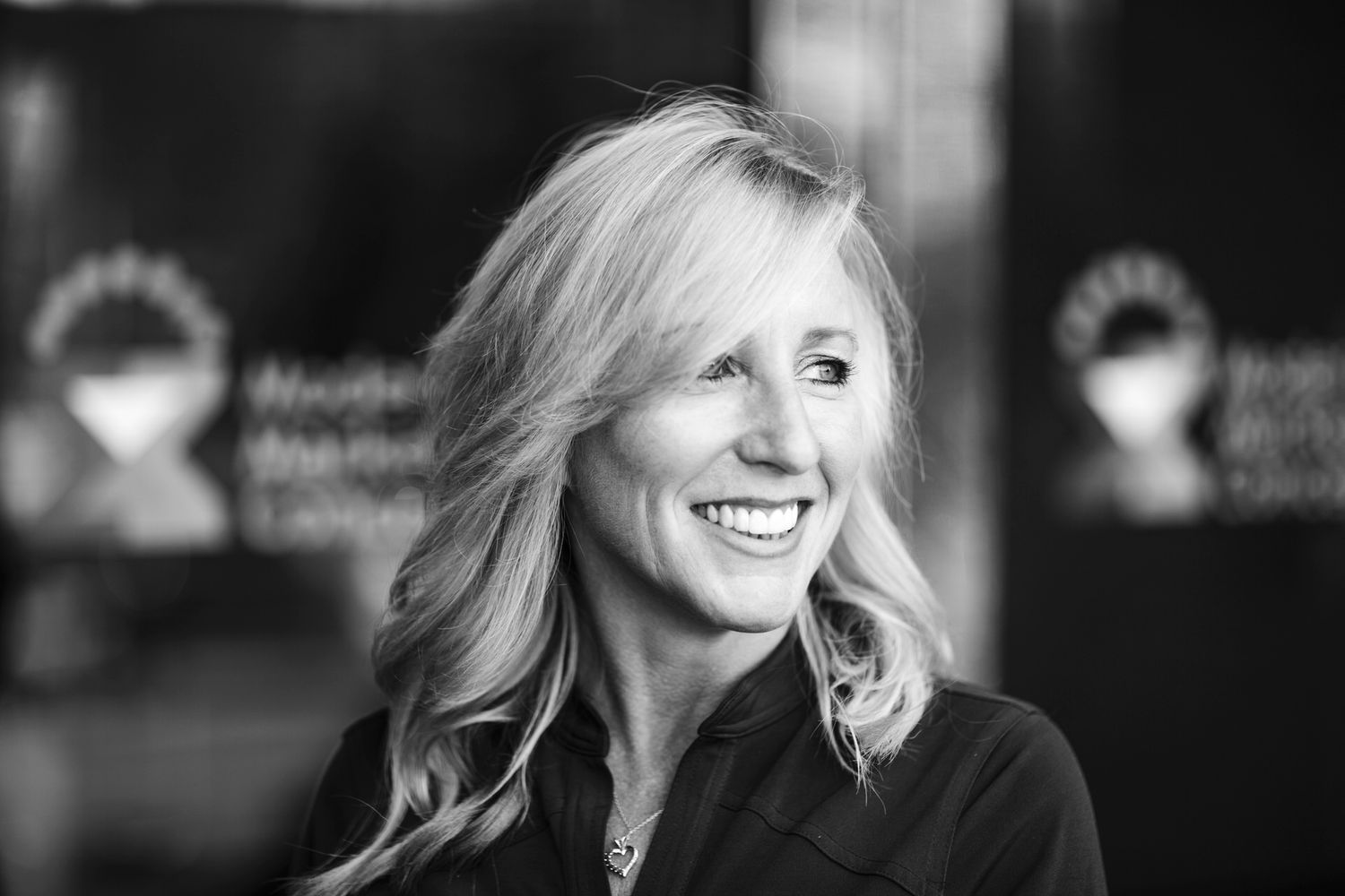 A black and white professional business headshot of a blonde woman smiling and looking to the right.