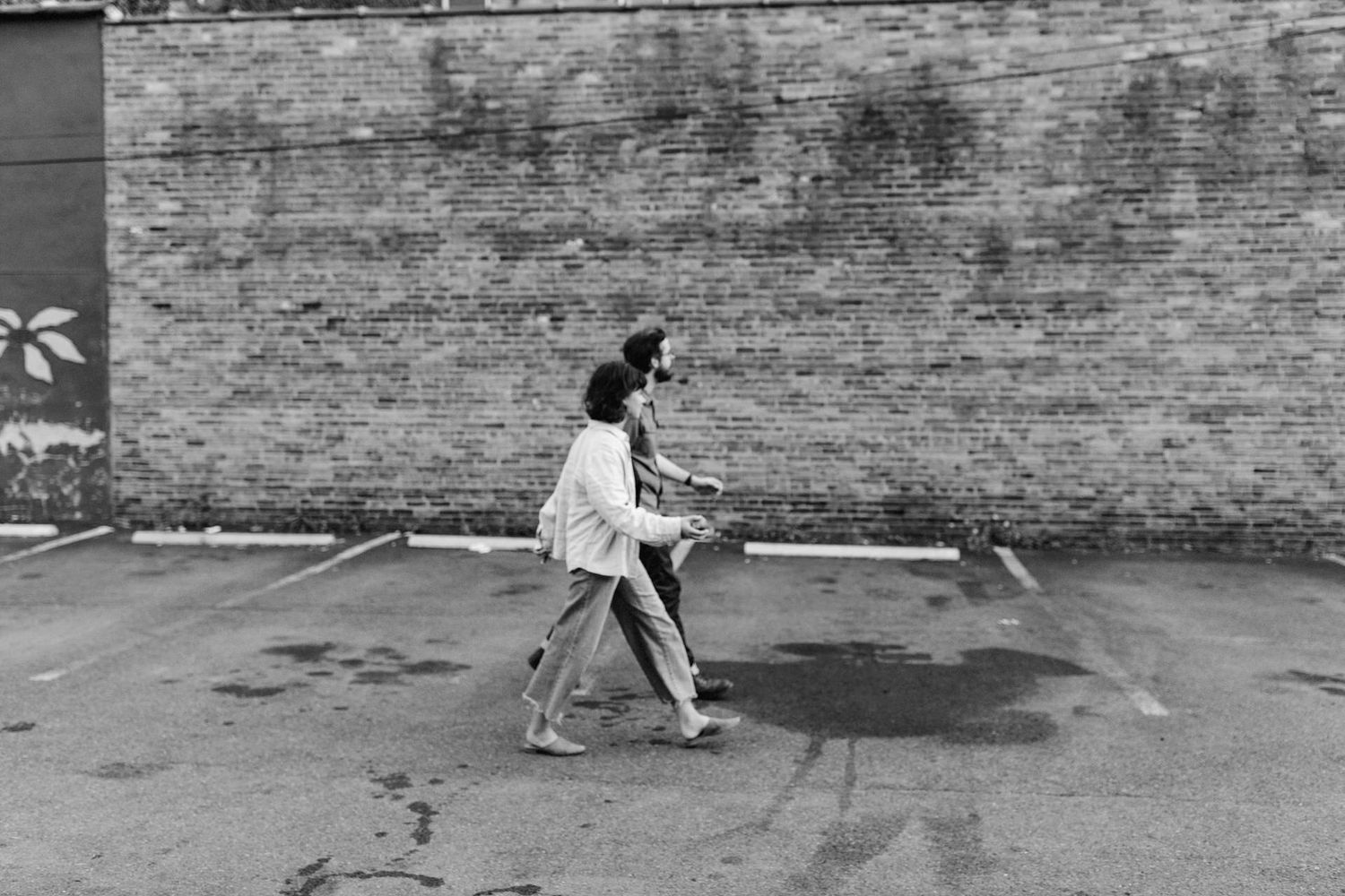 A black and white action shot of a pair of people walking in front of a brick building in downtown Troy, NY.
