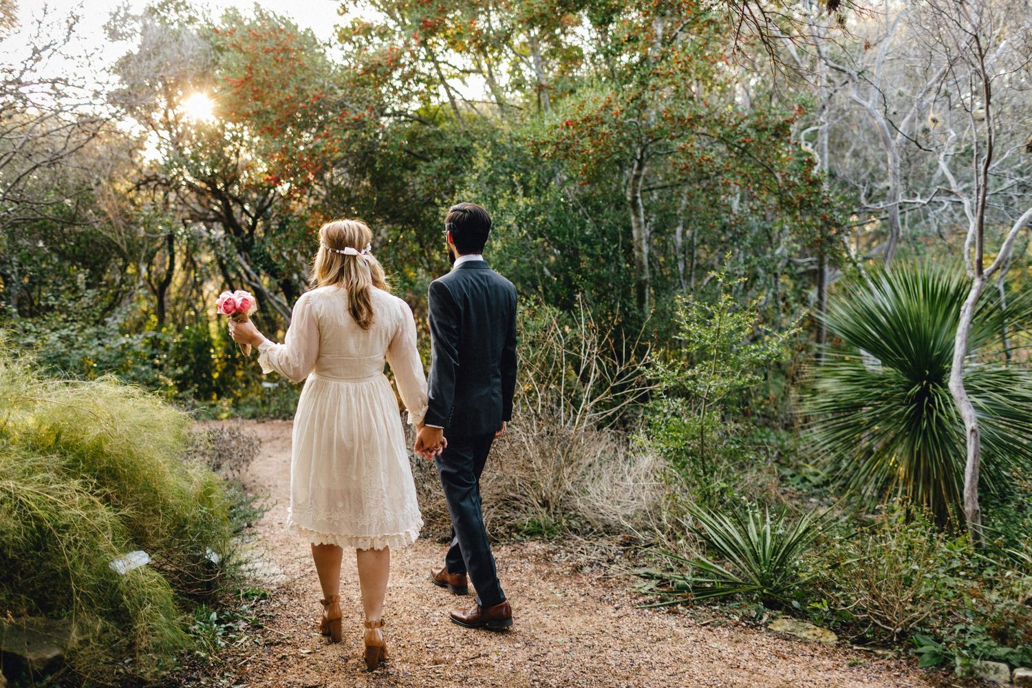 A photo of the back of a couple as they walk through the Austin Texas Botanic Garden in their elopement attire at sunset.