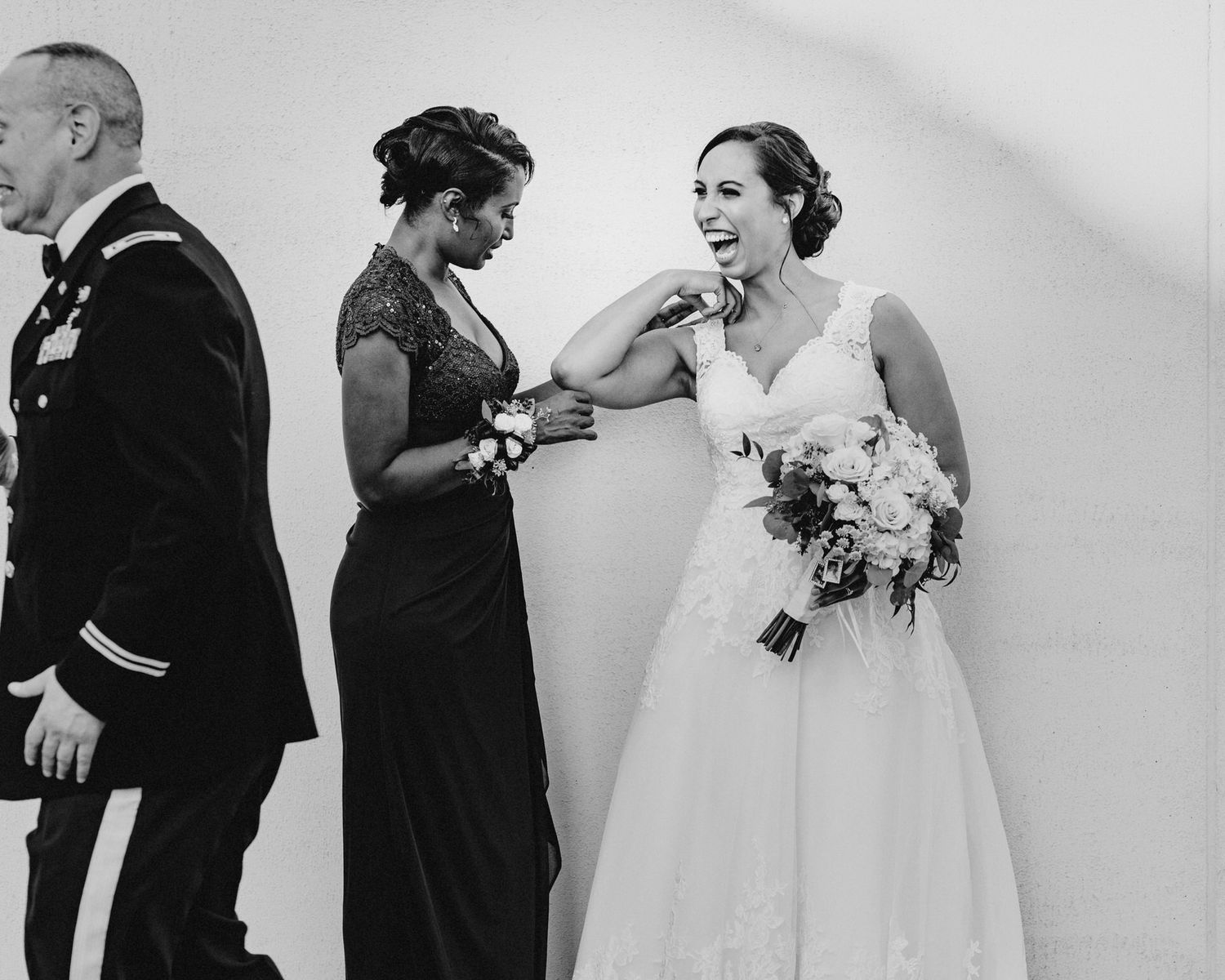 A black and white photo of a bride laughing while the mother of the bride and father of the bride rush to get out of the photo.