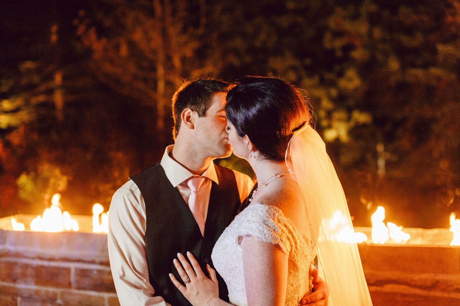 A wedding photo of a straight couple kissing in front of a ring of fire in New York.