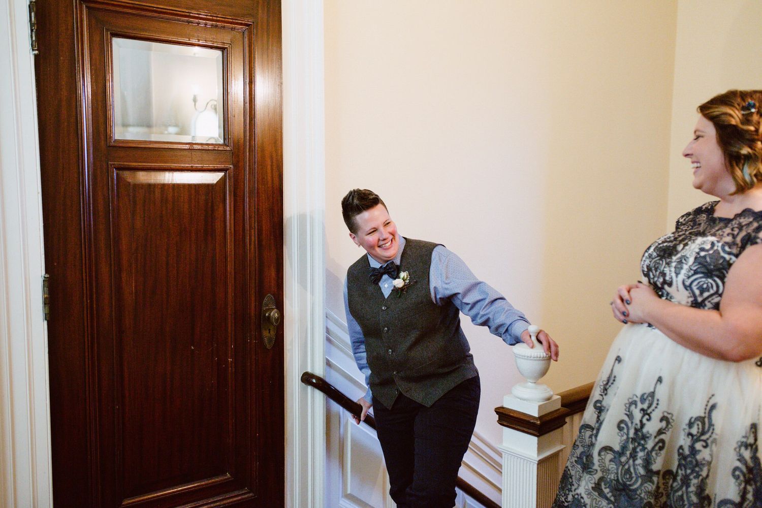 A first look at an elopement as a masc lesbian bride walks up the stairs to find her femme lesbian bride in her white and blue dress.