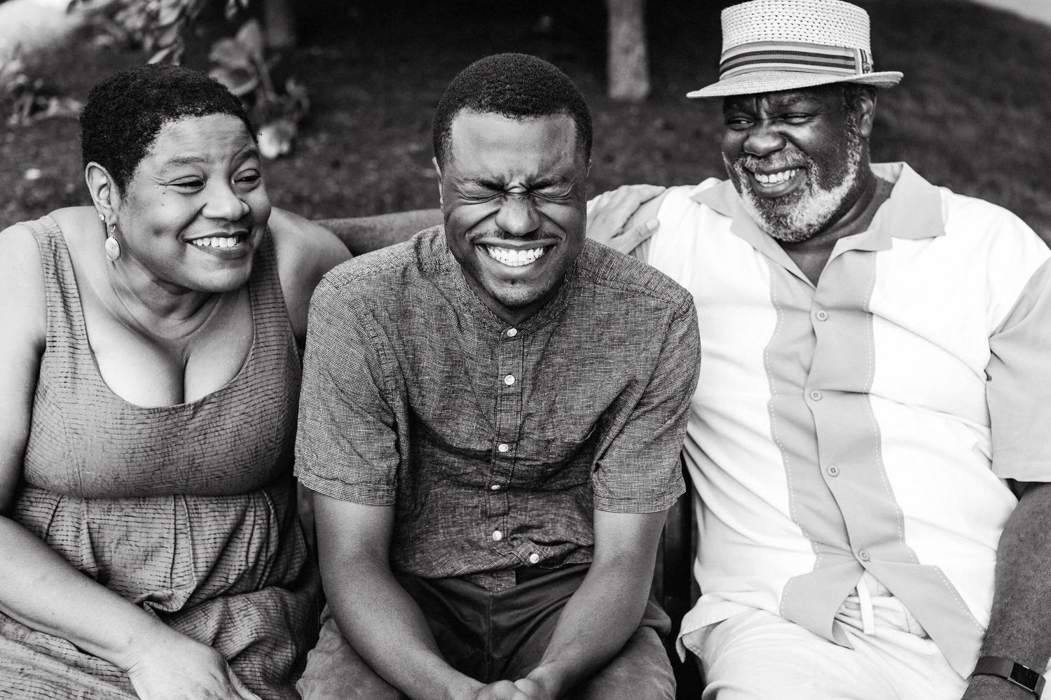 A black and white photograph of a Black family sitting on a bench in New York holding each other and laughing together.
