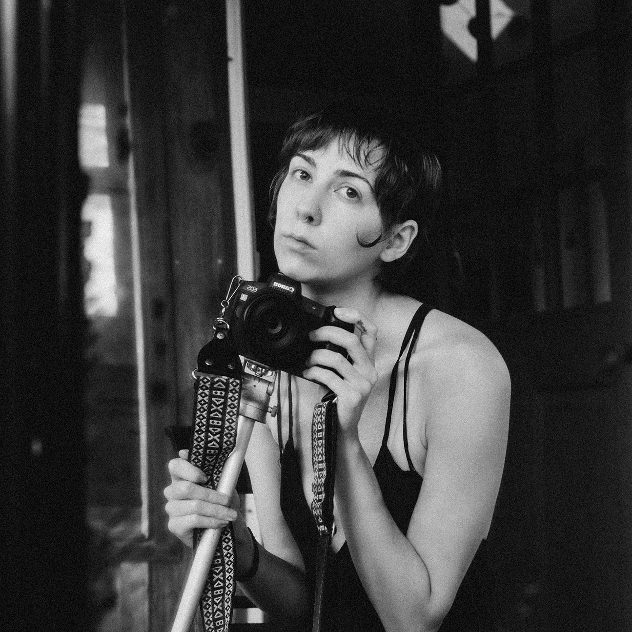 A black and white mirror selfie of Ro Tatchi and their camera listing on a tripod held under their chin.