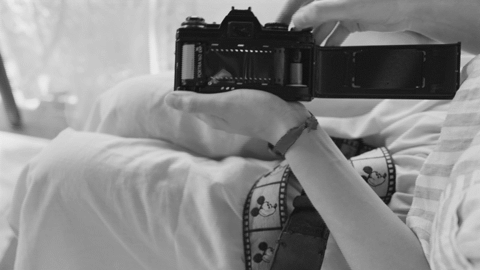 A black and white gif of Ro Tatchi loading a film camera and taking a picture.