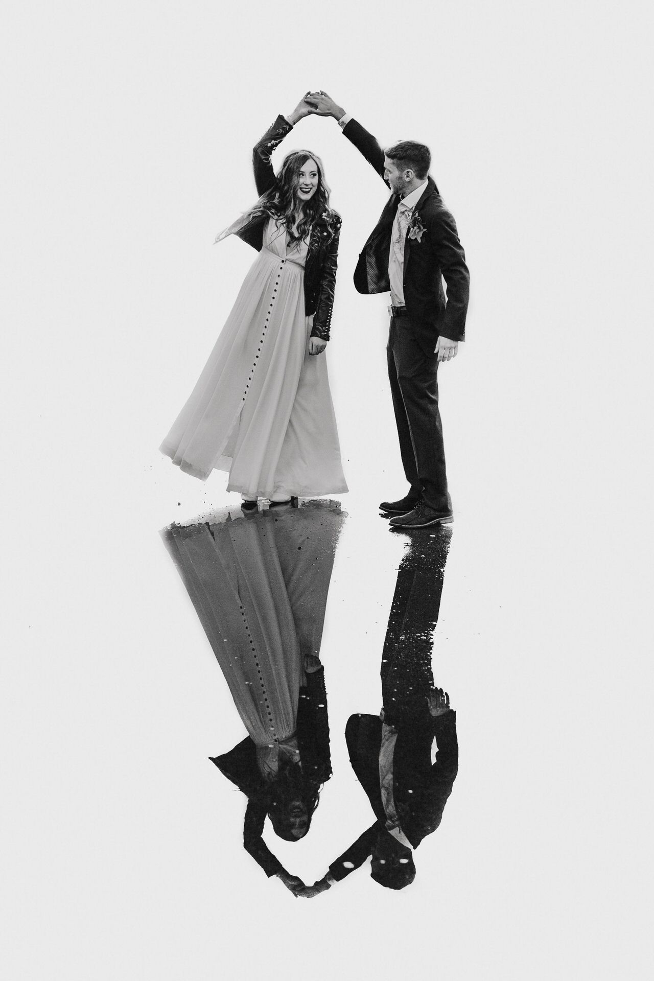 A black and white photo of a wedding couple spinning while standing on a giant puddle. The image shows them upright and perfectly reflected.