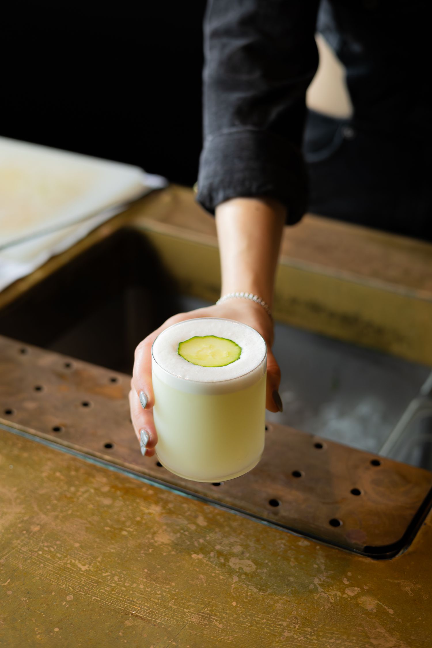A frosty white cocktail garnished with a lime wheel sits on a metal draining mat.