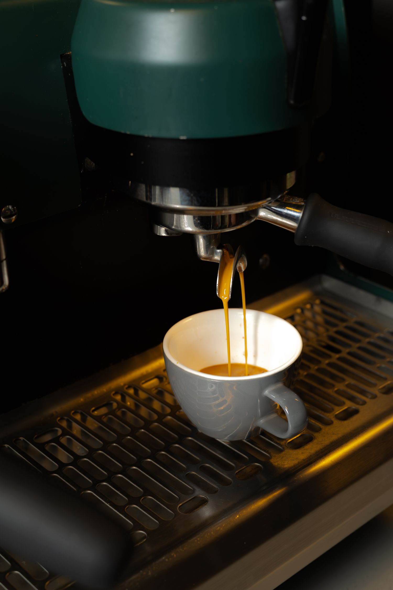 Espresso machine brewing fresh coffee into a white ceramic cup on metal grate.