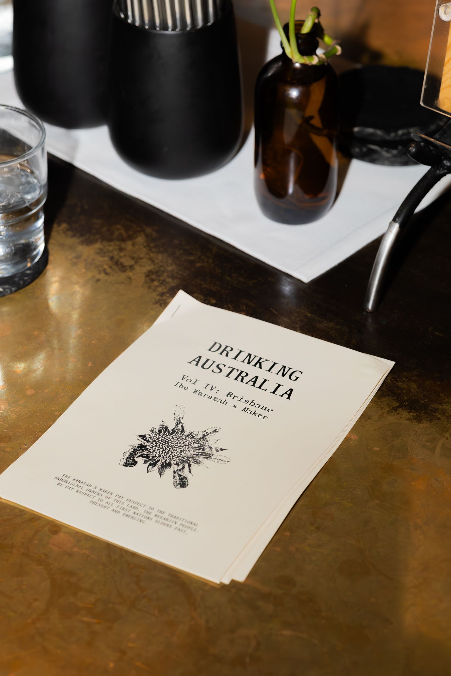 A 'Drinking Australia' menu or document displayed on a wooden table with bottles and glassware in the background.