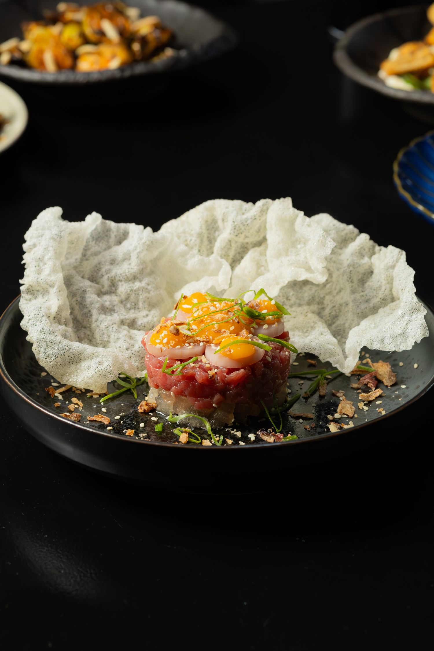 Tuna tartare with garnish served on crispy rice paper against dark background.