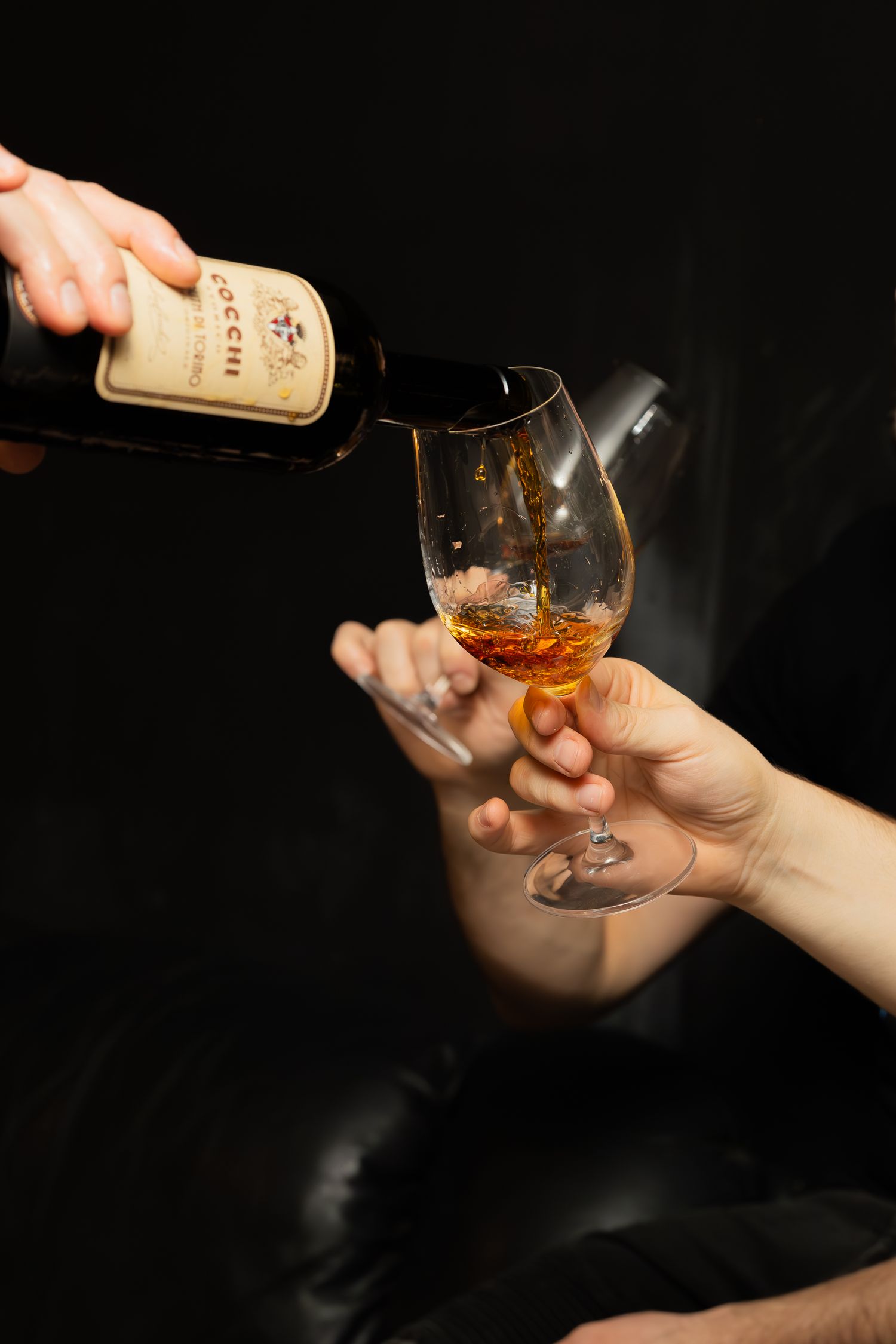Close-up shot of hands pouring amber liquor into a glass against dark background.