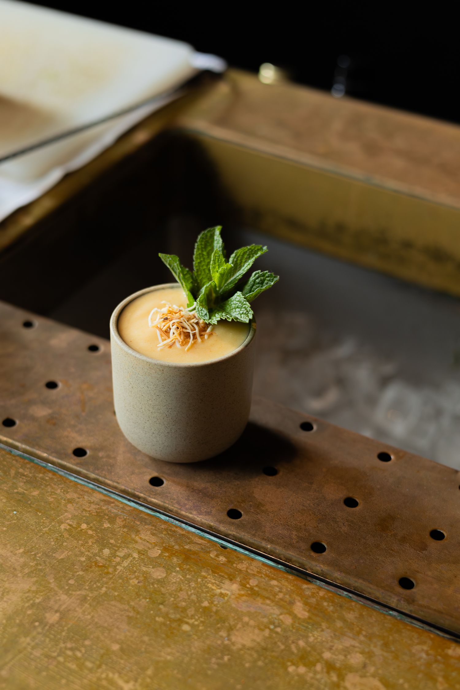 Cream colored cocktail in ceramic cup garnished with mint leaves.