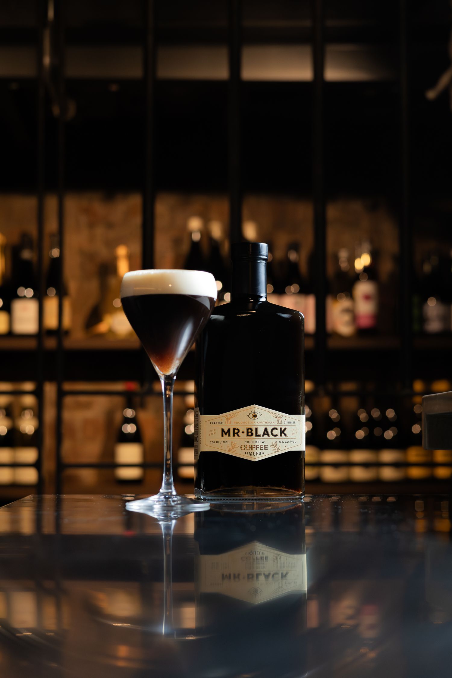 Elegant cocktail glass with Mr Black coffee liqueur bottle on dark bar counter.