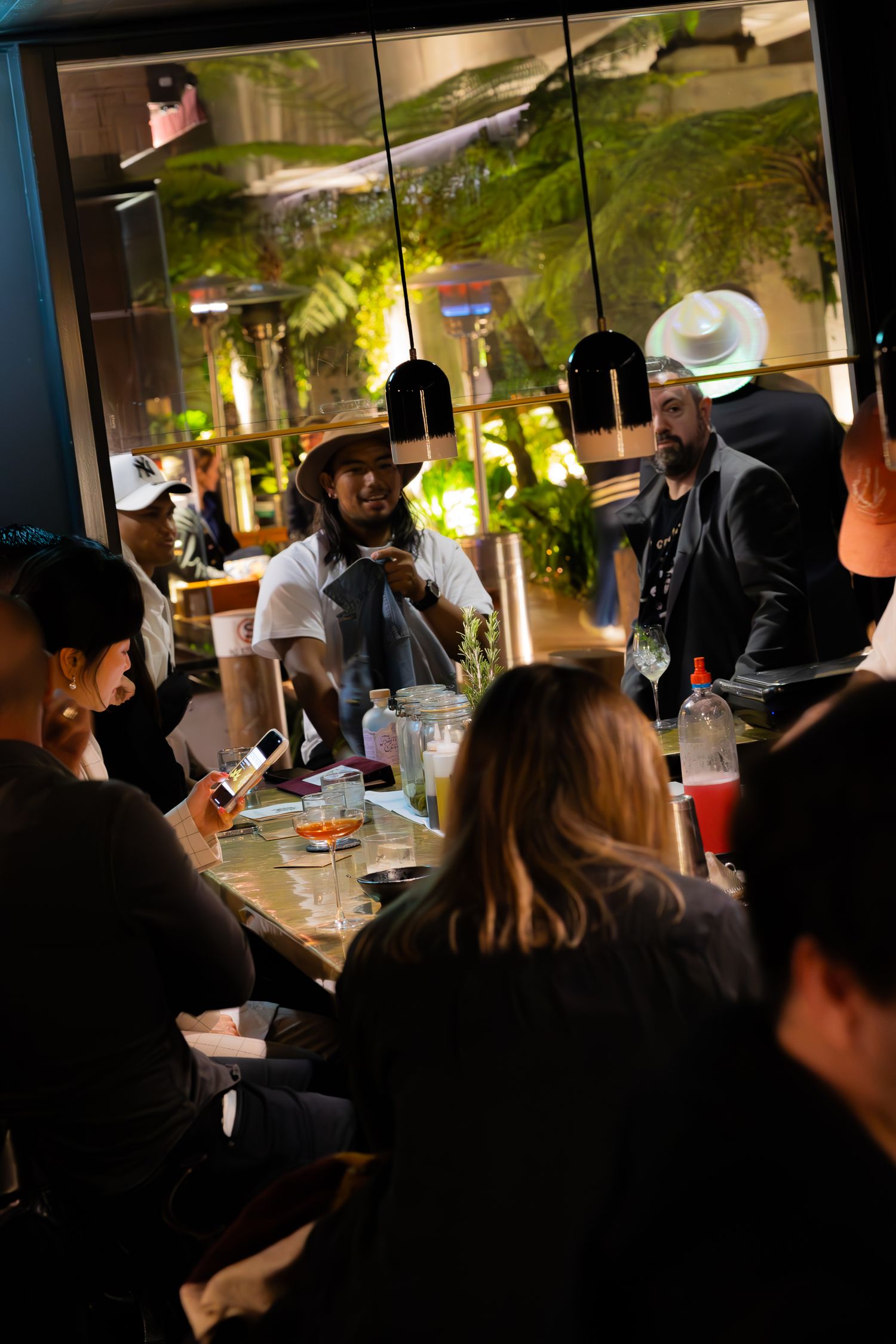 Crowded bar scene with pendant lights and tropical decor showing customers and staff interacting.